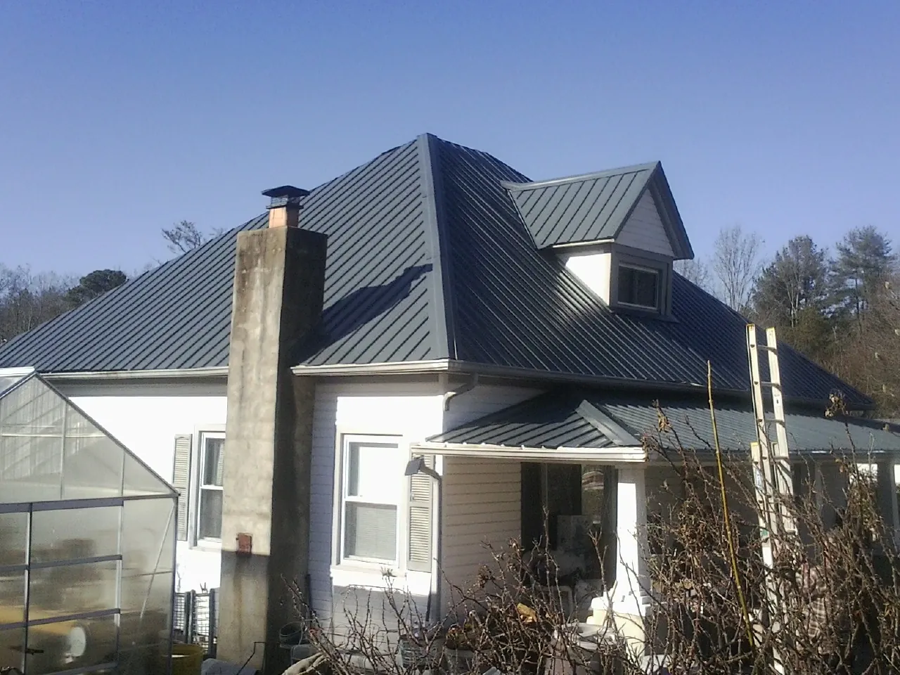 Dark blue standing seam metal roof on a white farmhouse with dormer — Slate & Tile Roof Repair by Roofing Brothers in East Norwich