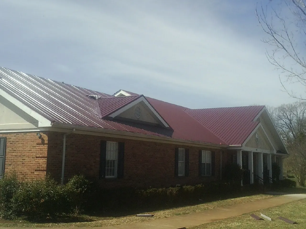 Red metal roof with gabled entries on a long brick building, from a Hail Damage Roof Repair job in East Norwich