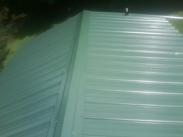 New green metal panels meeting at the ridge of a roof — Flat Roof Repair work by our crew in East Norwich