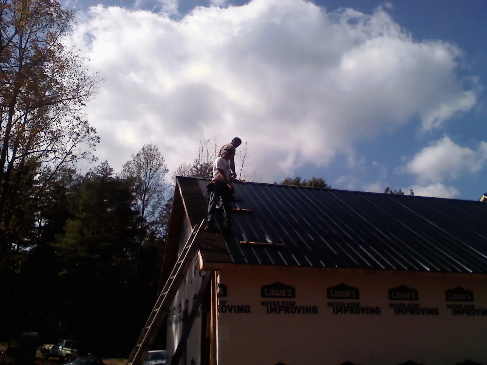 Roofer fastening dark metal panels high against a cloudy sky, from a Roof Inspection job in East Norwich