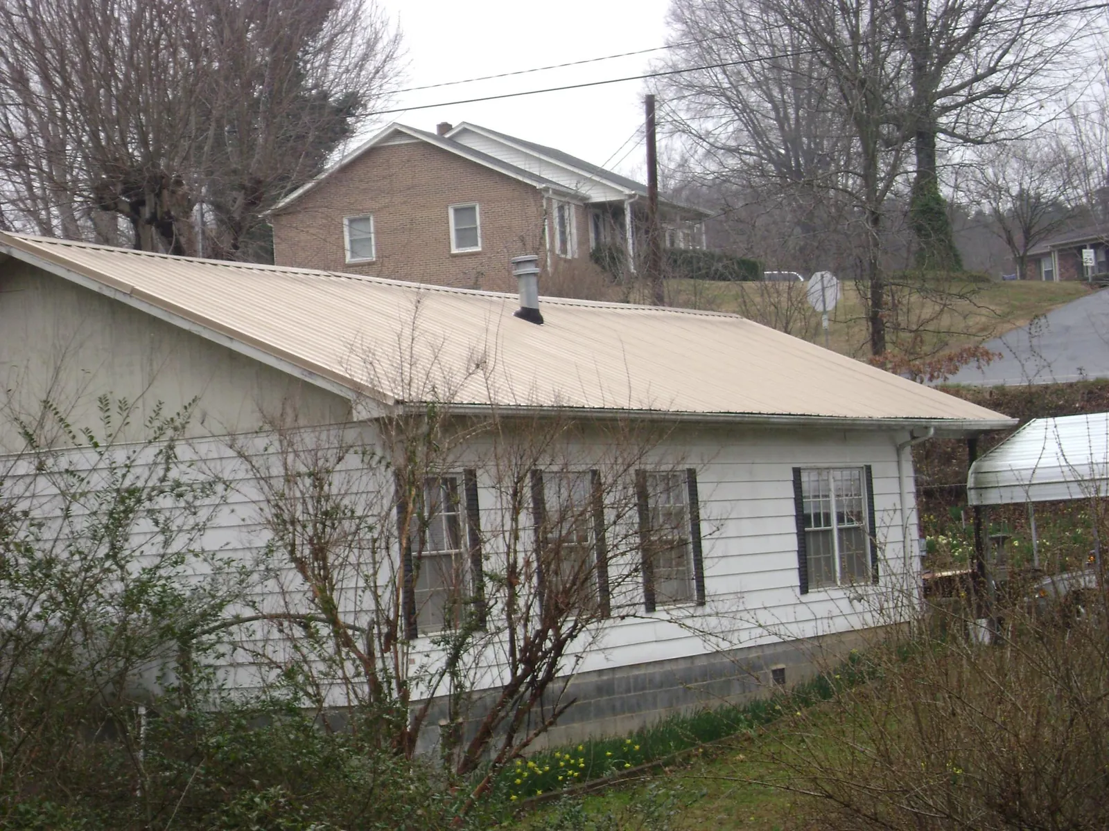 Tan metal roof on a white sided house set into a hillside — Commercial Roofing by Roofing Brothers in East Norwich